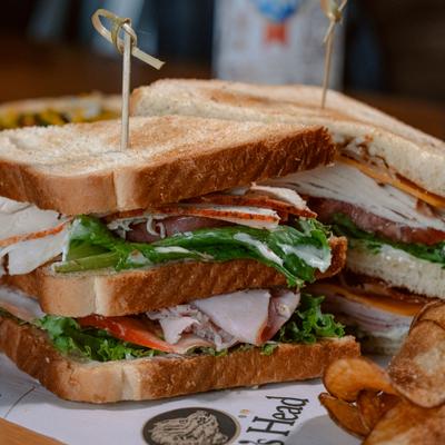 Stacked turkey sandwich with lettuce, tomato, and chips on the side.