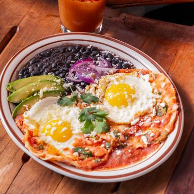 Huevos rancheros topped with fries eggs, served alongside black beans and avocado.