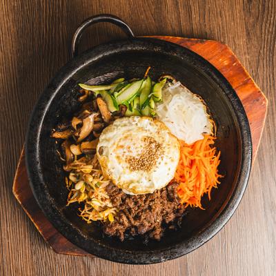 Hot Stone Bibimbap topped with assorted vegetables, beef, and a fried egg.