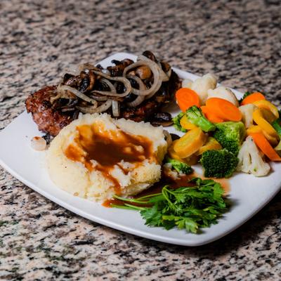 Steak topped with grilled onions, served with mashed potatoes and vegetables.