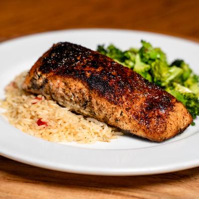 Blackened salmon served with rice and broccoli florets.