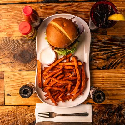 A burger served with sweet potato fries and a side of dipping sauce on a wooden table.
