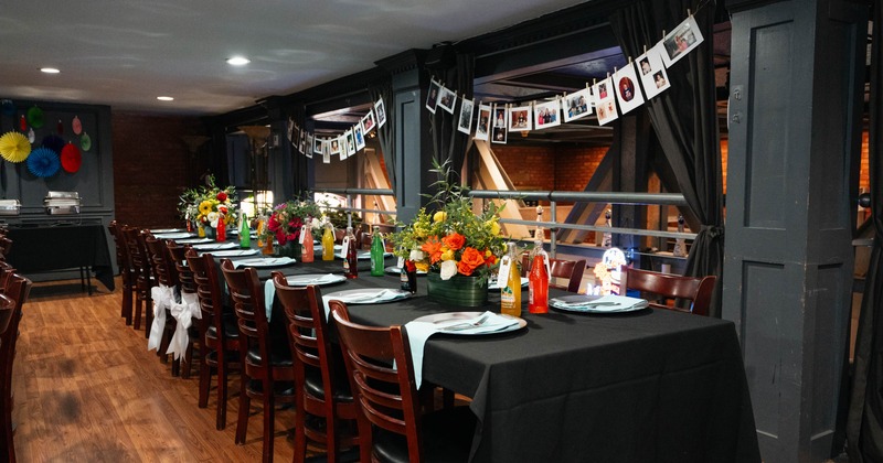 Inside, long table set for an event with floral centerpieces and hanging photographs