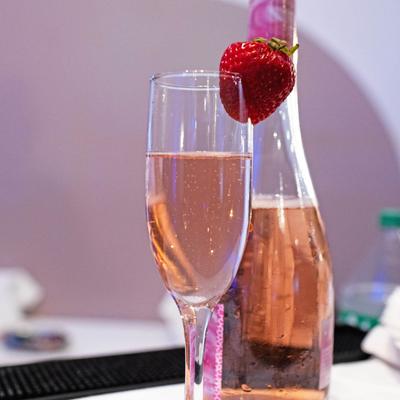 A glass of sparkling rose wine garnished with a strawberry.
