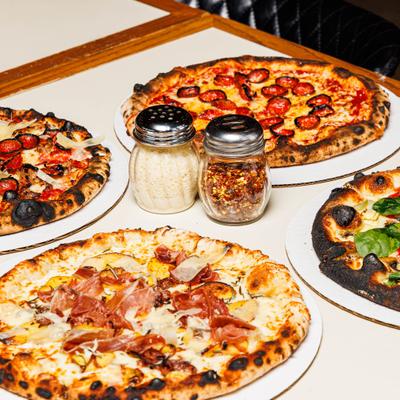 Selection of freshly baked pizzas served alongside condiment shakers.