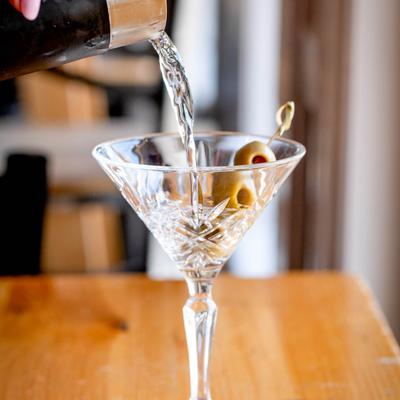 Martini being poured into a glass with olive garnish.