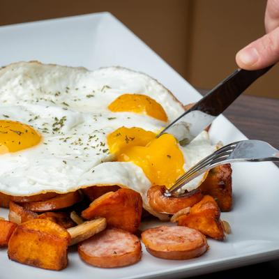 Hands holding knife and fork, cutting an egg.