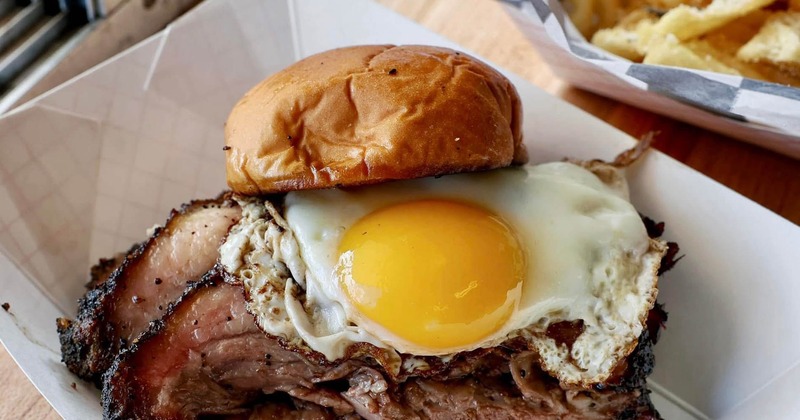 Brisket sandwich topped with a sunny-side-up egg, served with fries