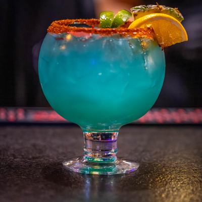 Spicy blue cocktail garnished with lime, pineapple, and orange slices.