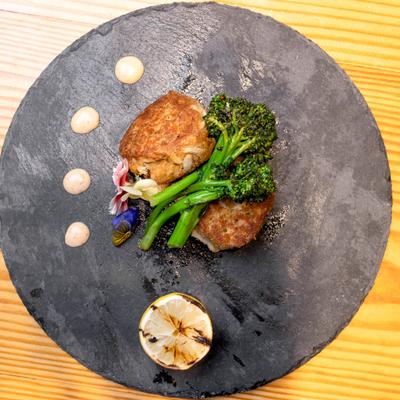 Crab cakes served with broccolini and a charred lemon on a slate plate.