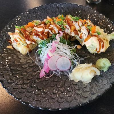 Plate of tempura sushi rolls drizzled with a sweet and savory sauce.