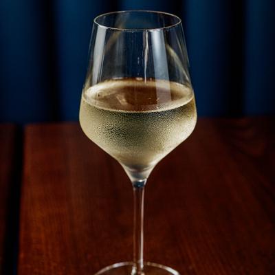 Glass of white wine on a dark wooden table with a dark blue background.