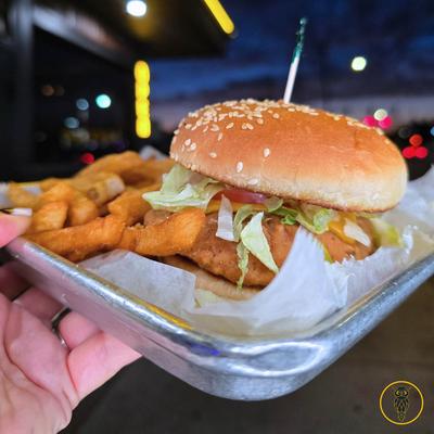Hand holding a plate with chicken sanwich and fries.