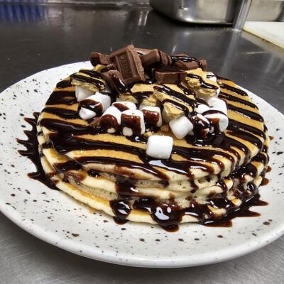 S'mores pancakes with Graham Crackers, Mini Marshmallows, Hershey's Chocolate Pieces and Drizzled with Chocolate Sauce.