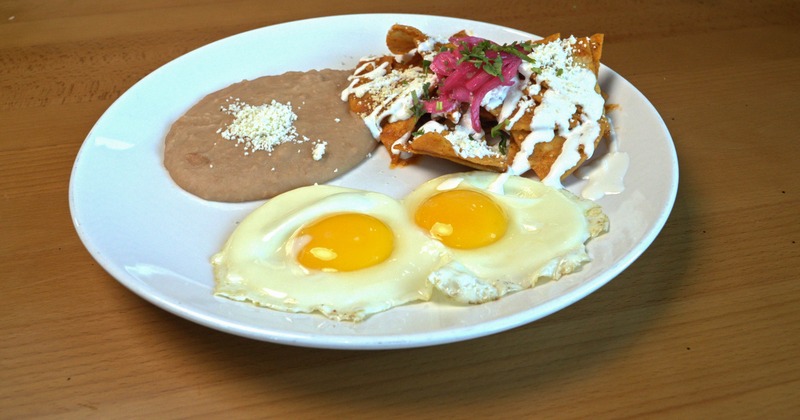 Tortilla chips smothered in red sauce, with sour cream, red onions, cheese, eggs, and beans
