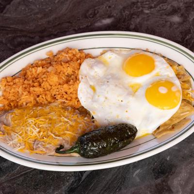 Corn tortilla chips smothered with sauce, topped with two eggs, sides of rice and beans.