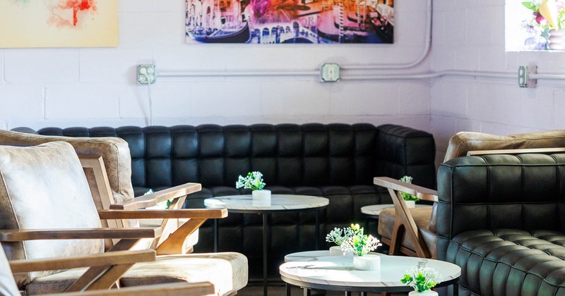 A cozy lounge with soft lighting features black leather couches and wooden armchairs