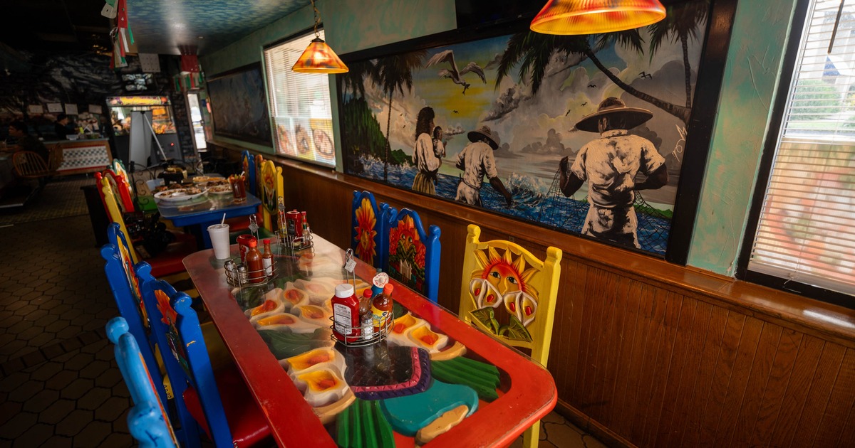 Colorful restaurant interior with a long artistic table, vibrant chairs, and a mural of fishermen on the wall