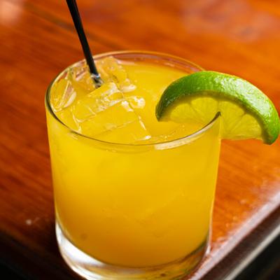 An orange cocktail on ice with a lime wedge and black straw.