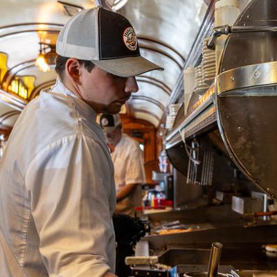 A chef in a white uniform and cap cooking in a bustling, warmly lit kitchen.
