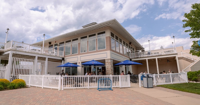 Restaurant exterior featuring a fenced patio with blue umbrellas under a cloudy sky