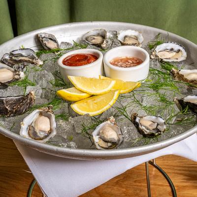 Fresh oysters on ice with champagne mignonette, cocktail sauce, and lemon wedges.