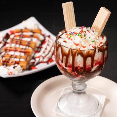 Ice Cream Sunday served in a glass goblet and a plate of churros in the background.