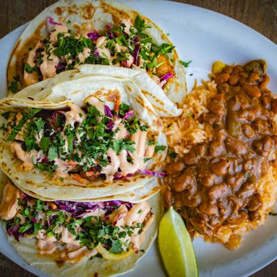 Plate of tacos with sides of rice and beans.