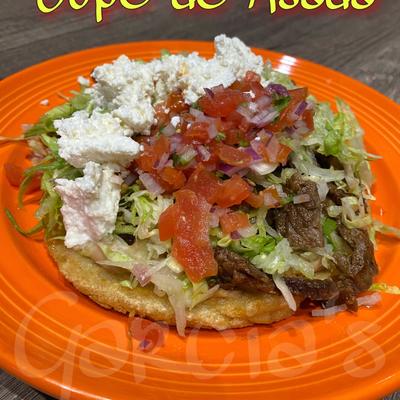 Sope topped with meat, lettuce, cheese, and salsa.