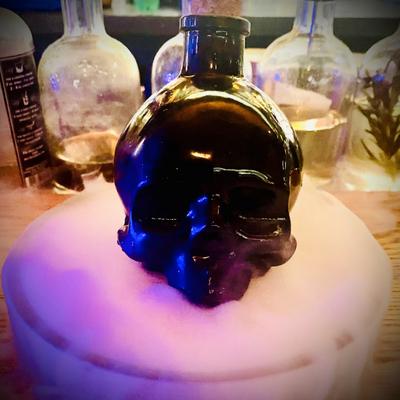 Corpse Survivor cocktail, served in a black skull bottle on a tray with smoking dry ice.
