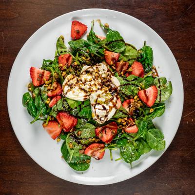 Spinach and burrata salad with strawberries, crushed pistachios, and balsamic drizzle.