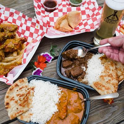 Assorted Indian dishes with curry, rice, naan, and beer on a table.