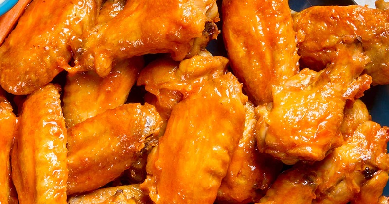 Buffalo-style chicken wings coated in a orange sauce, close-up