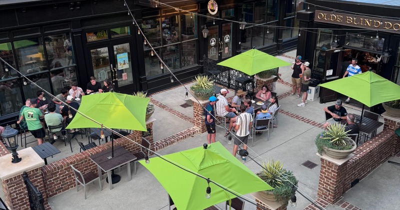 Outdoor patio with patrons enjoying drinks under bright green umbrellas