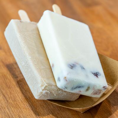 Two white ice cream paletas on a paper tray.