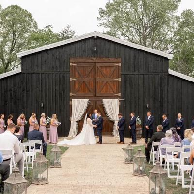 Outdoor wedding ceremony in front of a barn with a couple exchanging vows and guests.