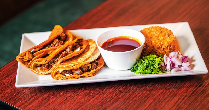 A plate of Queso Birria Tacos with consomme for dipping