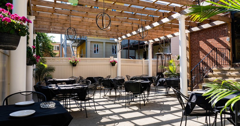 Outdoor dining area with black cloth tables and a wooden pergola adorned with pink flowers