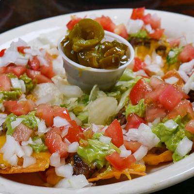 Loaded nachos topped with tomatoes, onions, guacamole, and jalapenos.