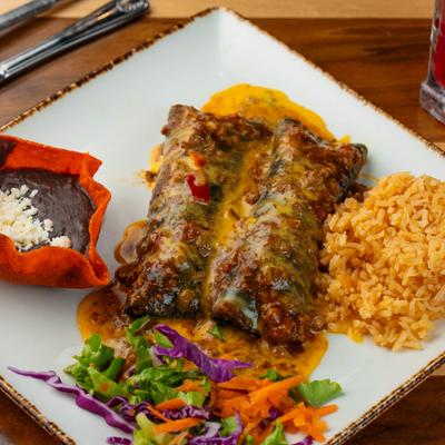 Two blue corn enchiladas topped with sauce and melted cheese served with rice, beans, and salad.