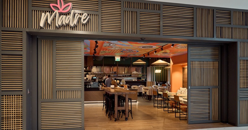 Entrance and interior of restaurant, wide view, tables and chairs behind, sign above