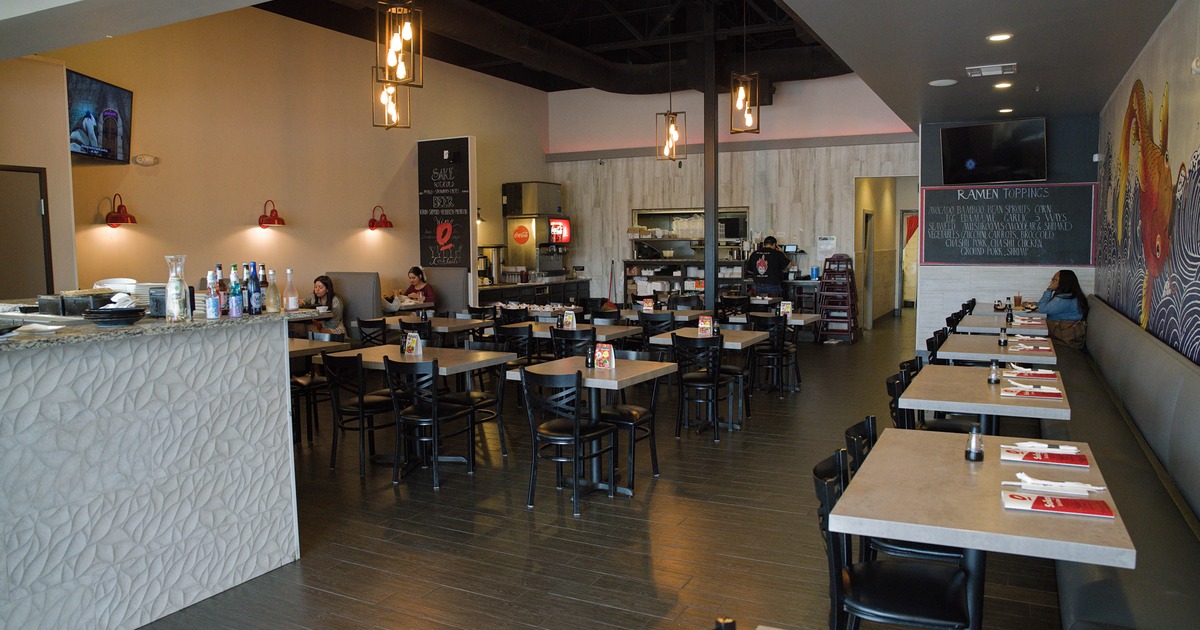 Contemporary restaurant interior with tables, black chairs, pendant lights, and a textured counter