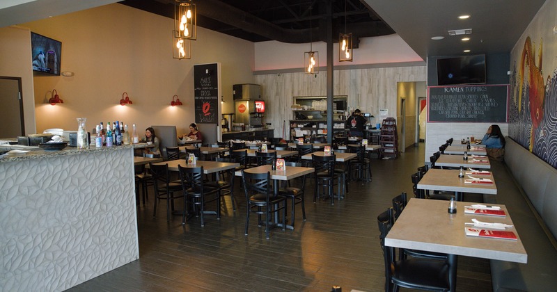 Contemporary restaurant interior with tables, black chairs, pendant lights, and a textured counter