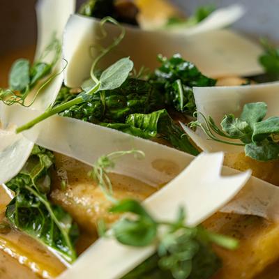 Butternut squash raviolo topped with shaved Parmesan and microgreens.
