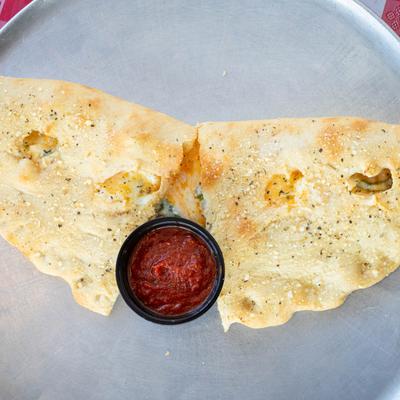 A halved calzone and marinara sauce.