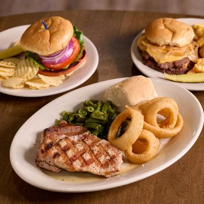 Grilled chicken plate served alongside two burgers with sides.