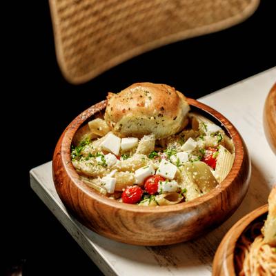 Penne pasta salad with feta, tomatoes, and garlic bread in wooden bowls.