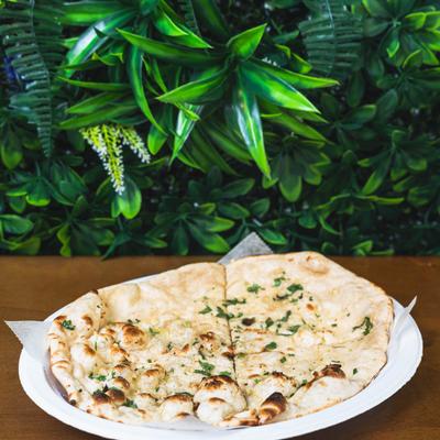 Garlic naan on a wooden table with green foliage in the background.