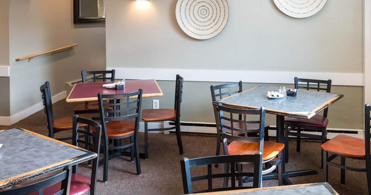 Interior dining area with tables and chairs, decorative plates on wall and an arched doorway
