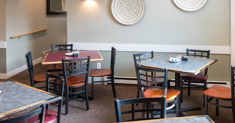 Interior dining area with tables and chairs, decorative plates on wall and an arched doorway